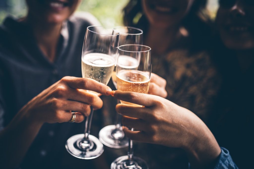 Three female friends celebrating with champagne. They are sitting in a bar and toasting with glasses of champagne.