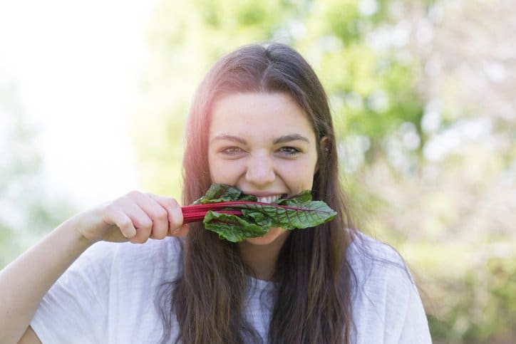 A girl biting a leaf of raw ruby red chard