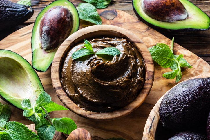 Raw avocado chocolate mousse pudding with mint in olive wooden bowl. Vegan vegetarian food. Organic healthy dessert