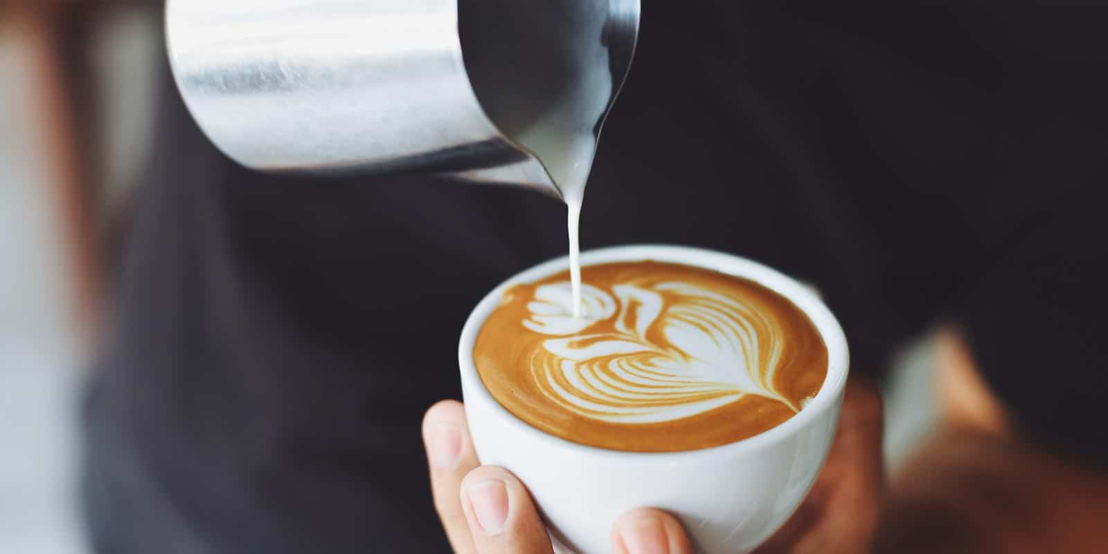 A photograph of a barista pouring milk into a coffee.